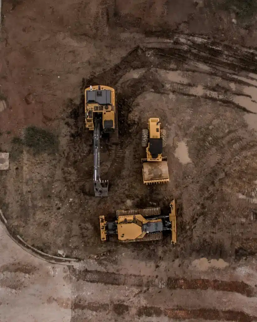 Aerial view of construction site with three bulldozer trucks on bare ground